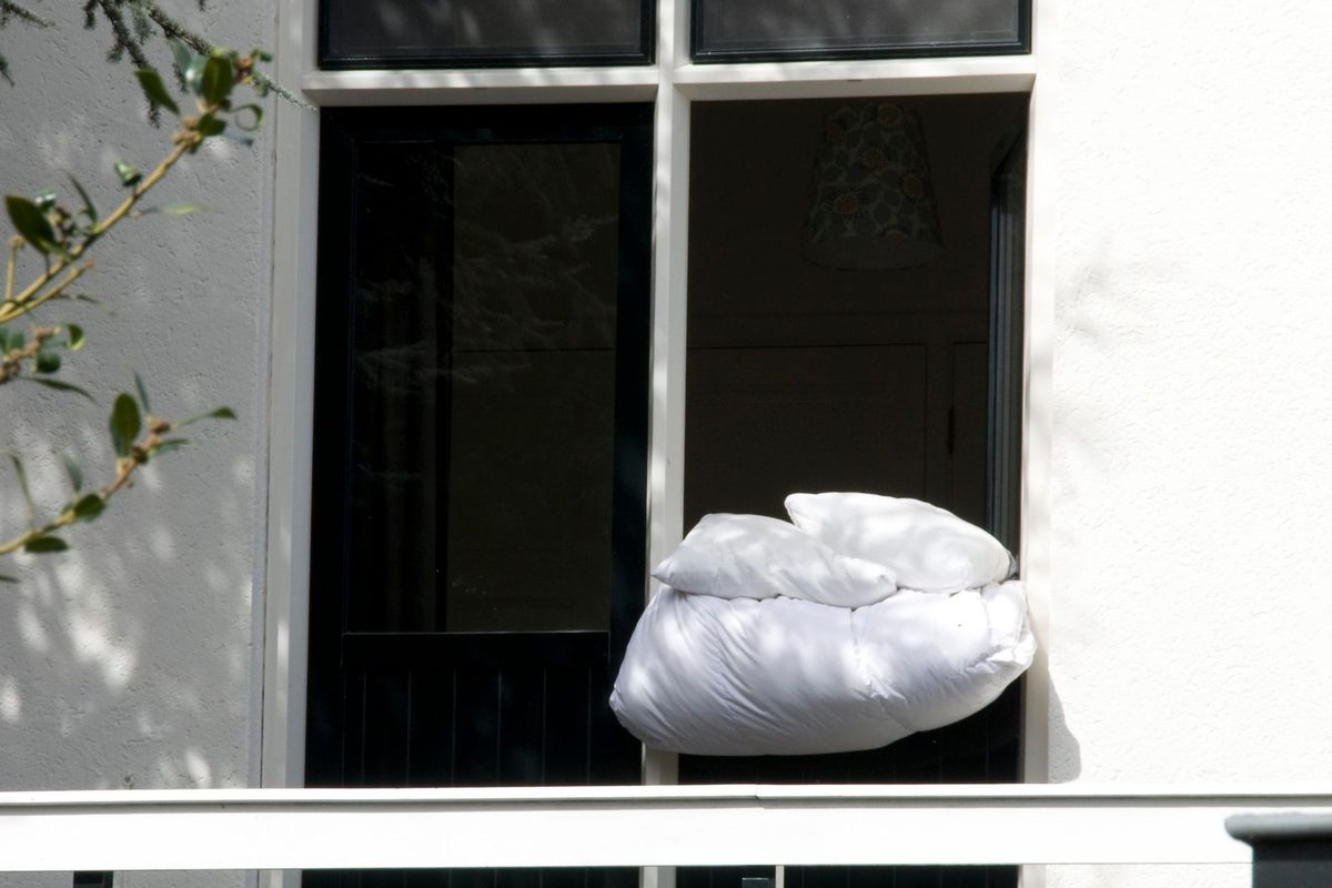 A pillow and a duvet airing on an open window ledge in the sun