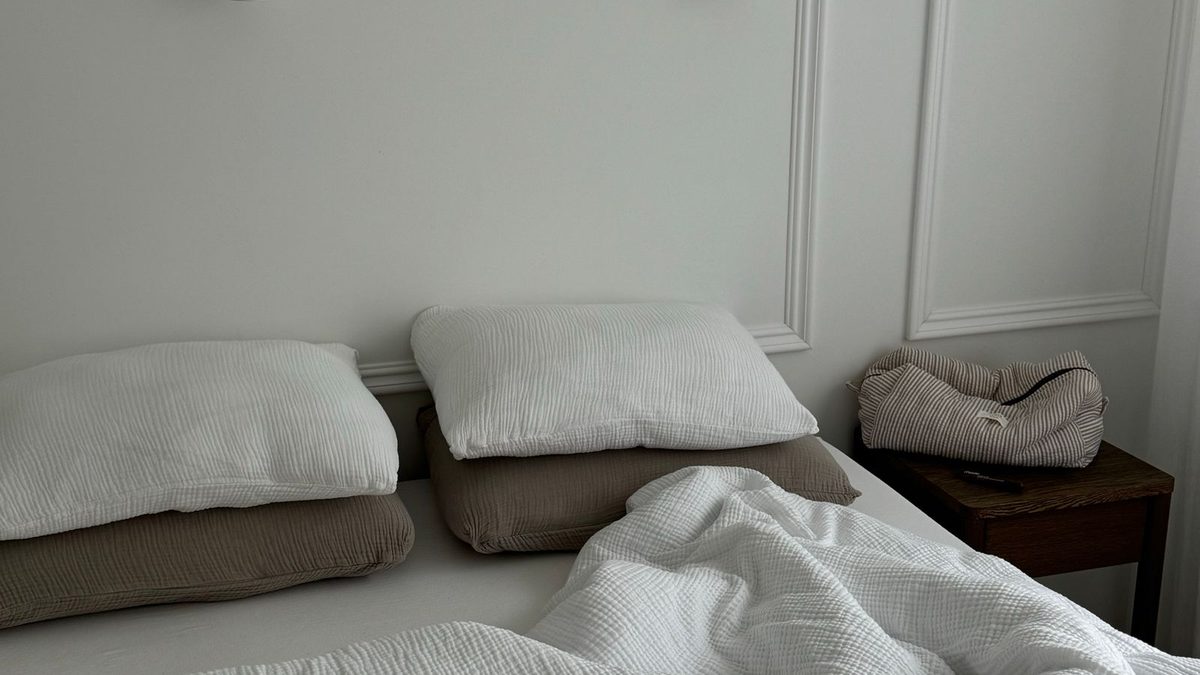 A bed made up in white with two pillows against a pale panelled wall